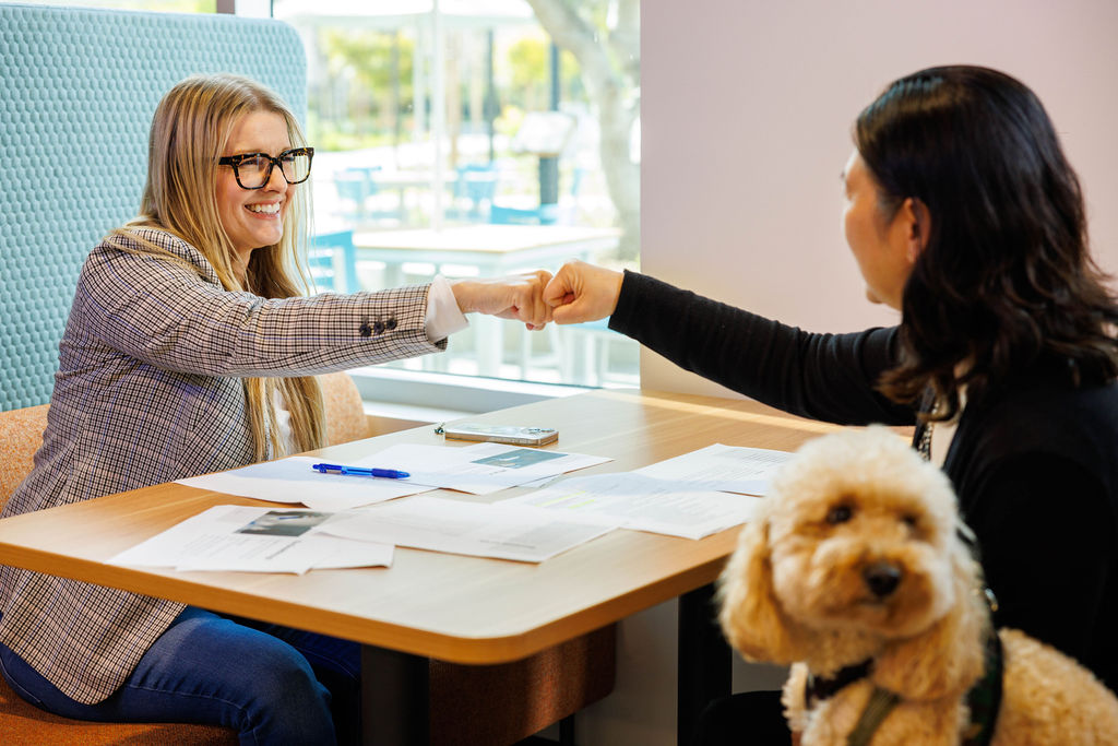 Two Crinetics employees collaborating at a desk with a dog in the foreground